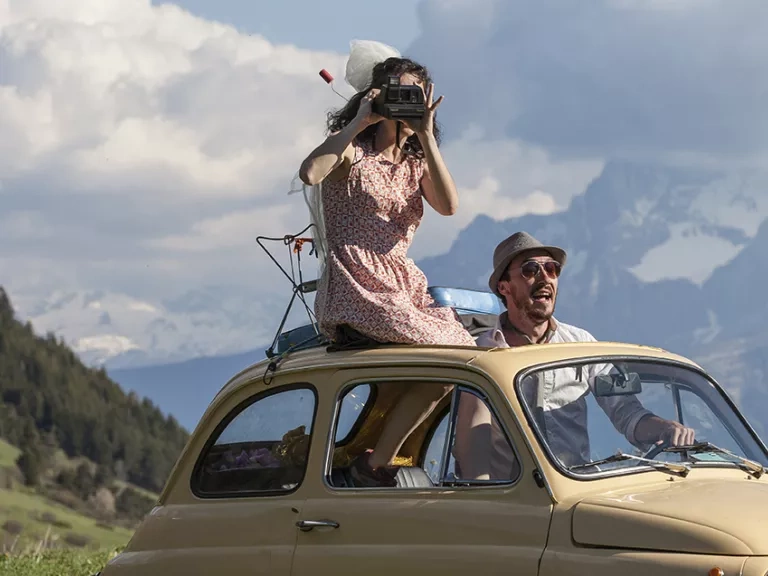 Une femme et un homme debout dans une Fiat 500 décapotée. En toile de fond la montagne © Jean-Pierre Angéi